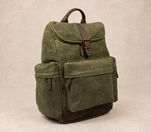 Olive green textile backpack with dark brown leather trim, AIL-BP-0013, shown from a front three-quarter angle on a warm limestone studio background
