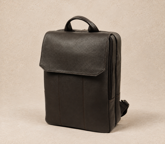 Dark brown pebbled leather backpack AIL-BP-0015, shown from a front three-quarter angle on a warm limestone studio background