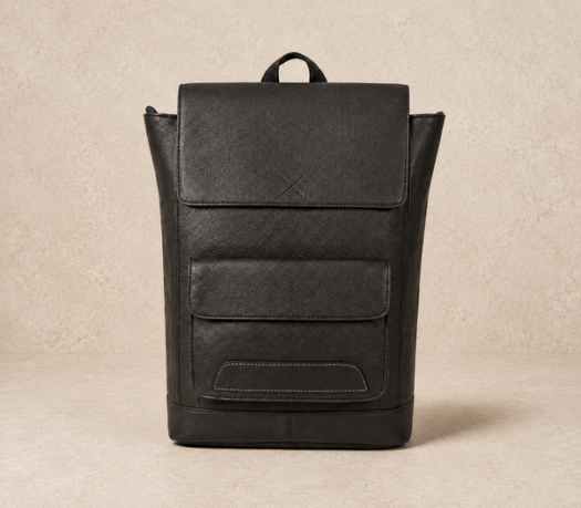 Black pebbled leather backpack AIL-BP-0018, shown from the front on a warm limestone studio background
